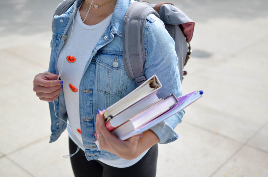 Woman in a denim jacket listening to earbuds and carrying college books
